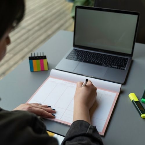 A doctor sitting at a desk planning out a timed GSSE mock exam with markers and a laptop.